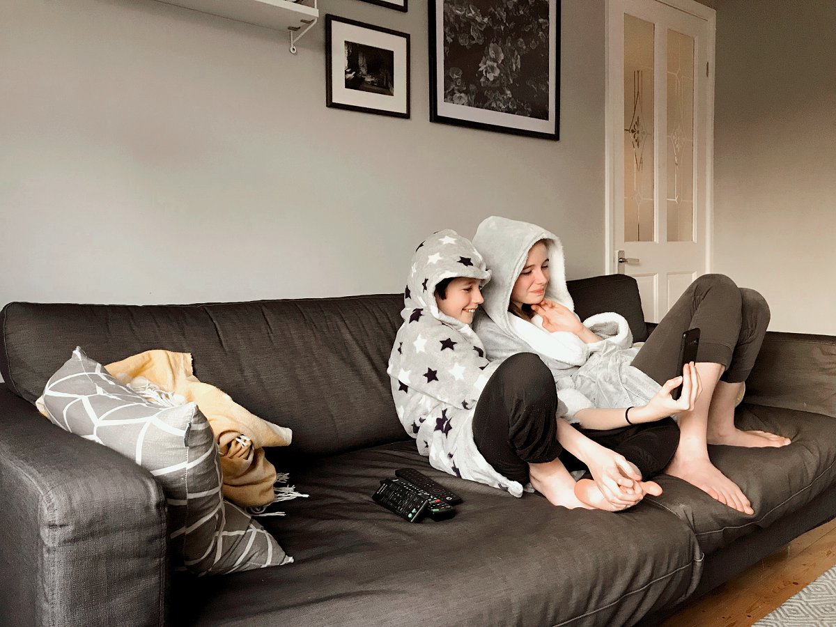 Children in pyjamas and dressing gowns take a video call curled up on the sofa